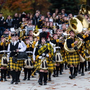 Ƶ marching band marches in uniform with alumni and families trailing behind.